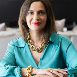 A woman wearing a blue shirt and gold necklace.
