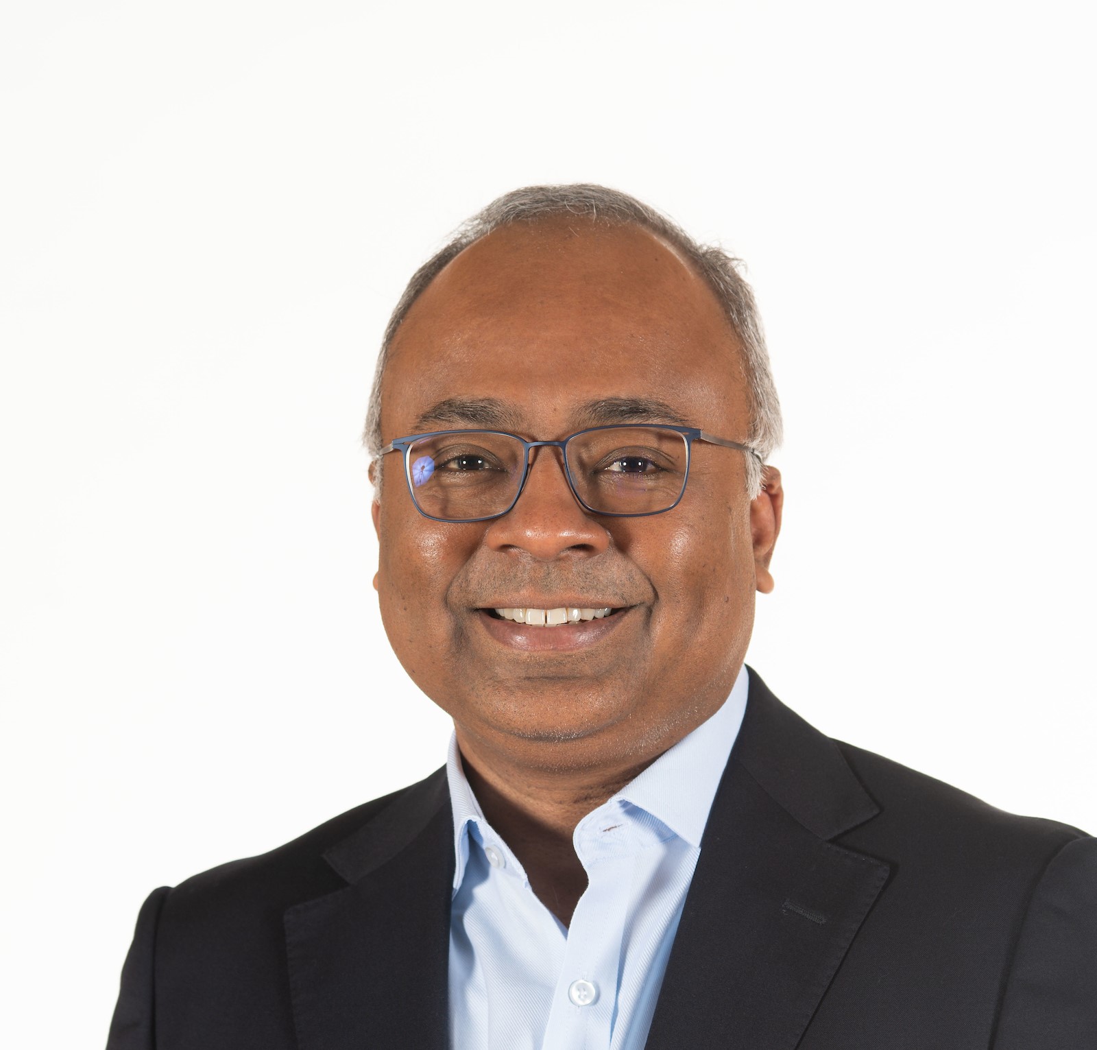 An indian man wearing glasses and a blue shirt.