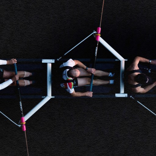 A group of people collaborating and showcasing trust as they sit together on a rope, against a captivating black background.