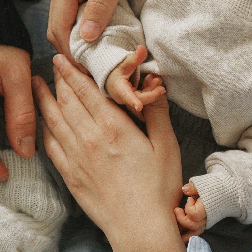 A woman holding a baby's hand, symbolizing the bond between families.