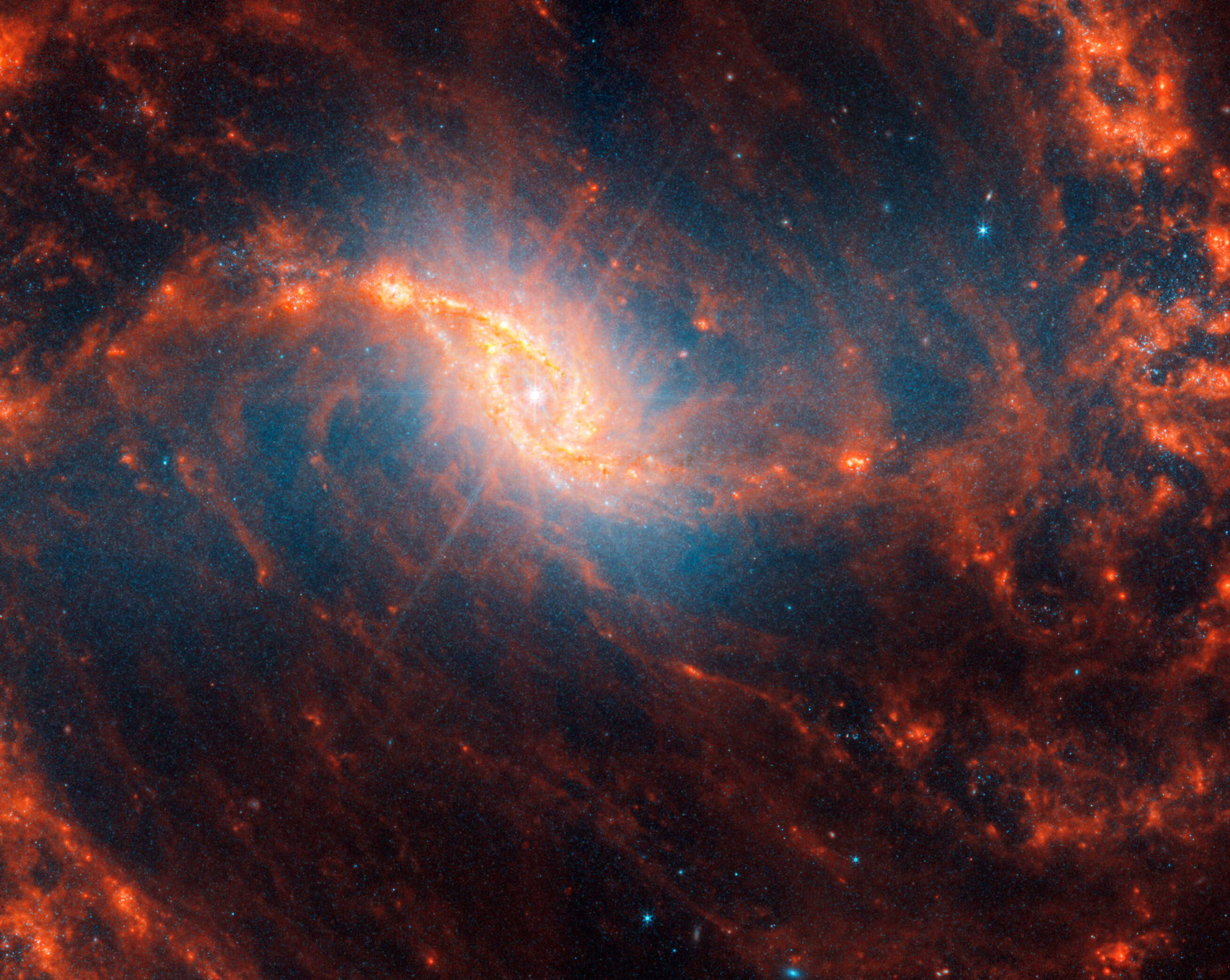 Webb&rsquo;s image of galaxy NGC 1365 shows a central region that looks like an angled, smashed oval that is a mix of bright orange shades that emanate a blue glow. The galaxy&rsquo;s bar extends horizontally from the oval. It is crossed by messy dust filaments that curve slightly, forming a backward S shape. Fainter filaments appear below and above the core.