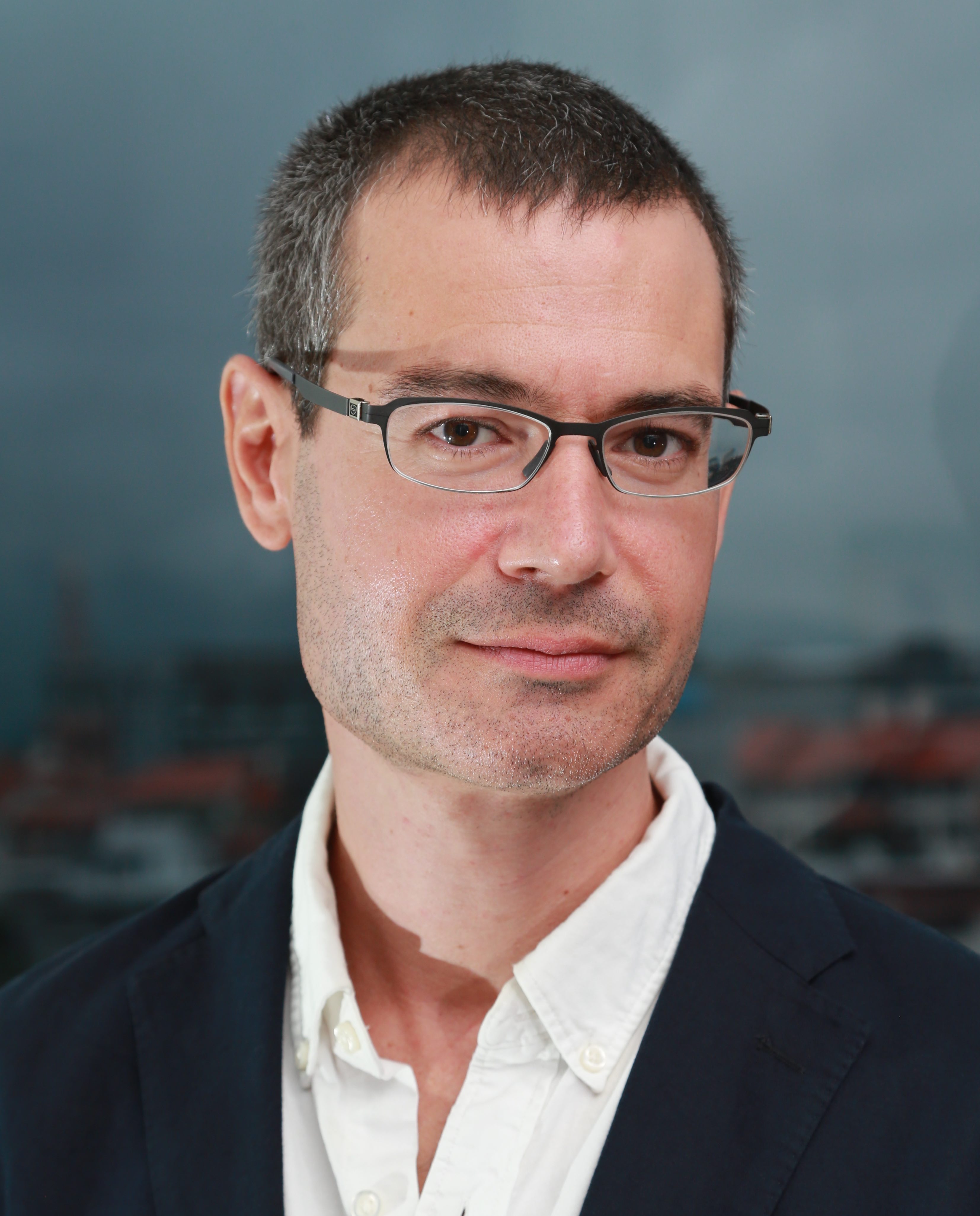 A man in glasses is standing in front of a city.