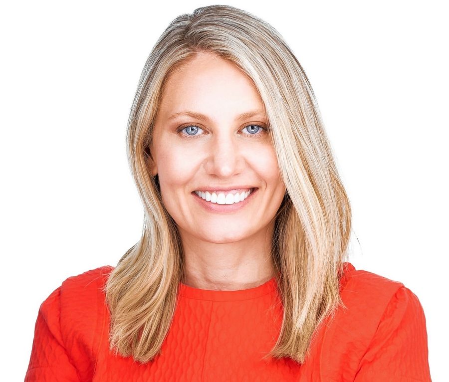 Woman with blonde hair wearing a red top smiling against a white background.