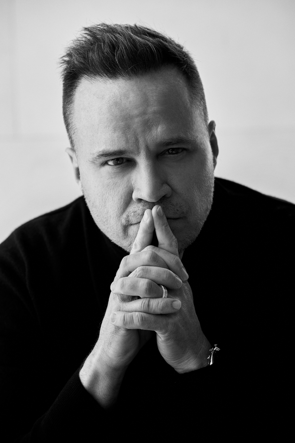 A black and white photo of a man posing with his hands in his pockets.
