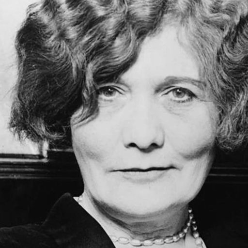 Black and white portrait of a smiling woman with wavy hair and a pearl necklace, circa early 20th century.