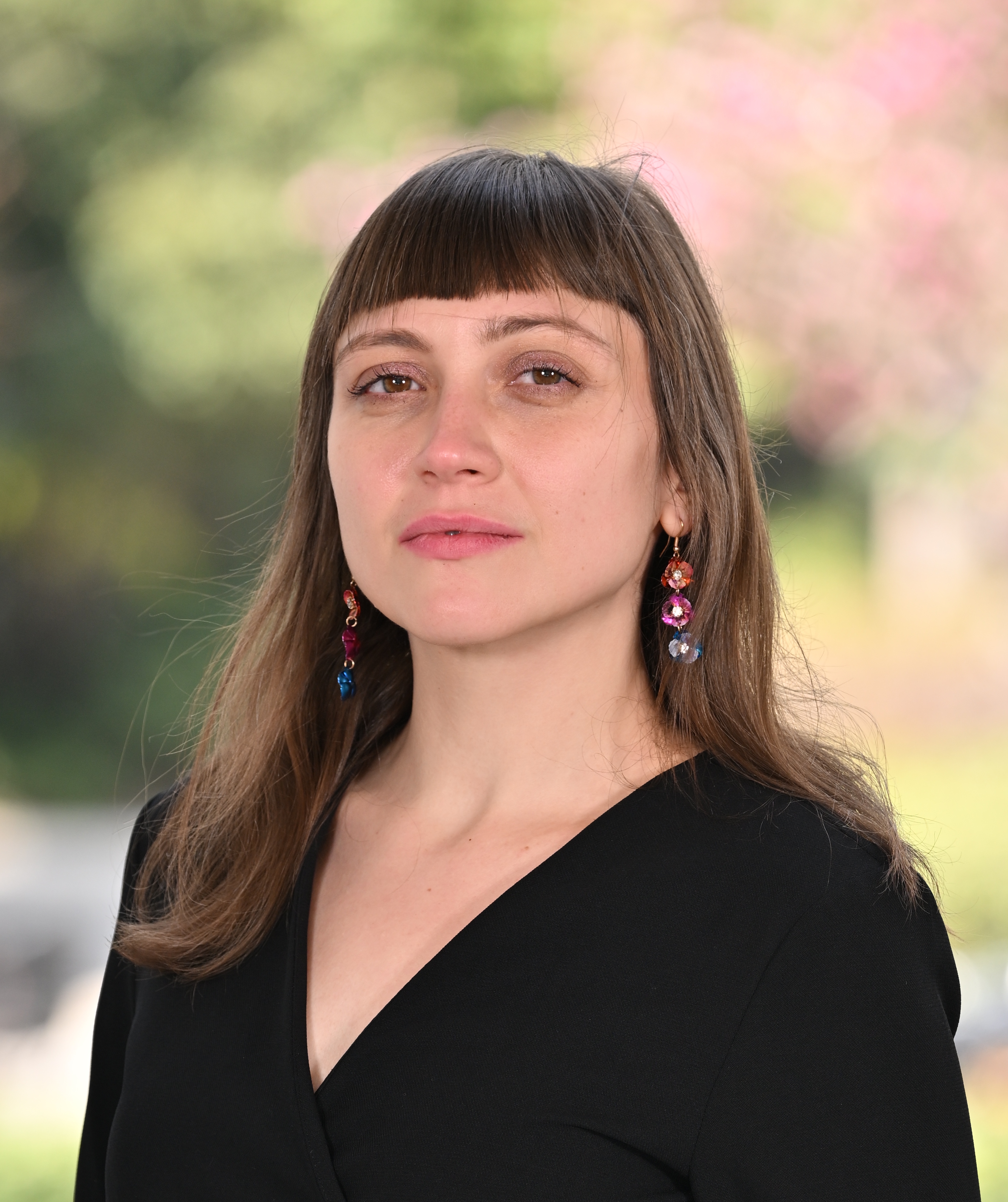 Woman with bangs wearing earrings and a black top posing for the camera.