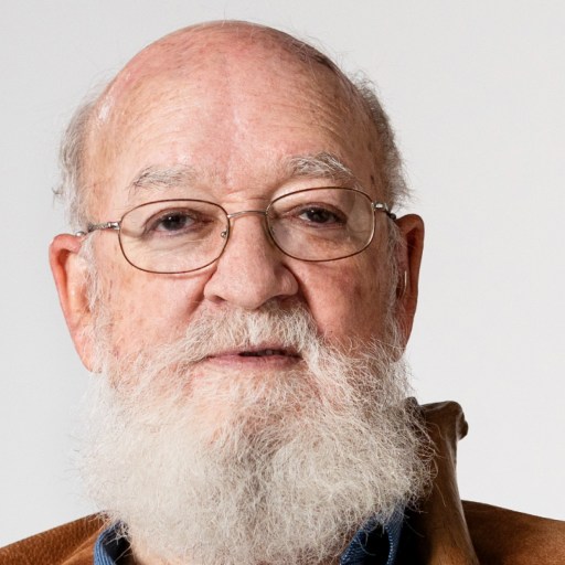 Elderly man with a full white beard and glasses, wearing a brown jacket, against a white background.