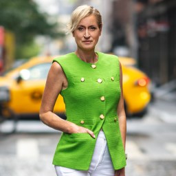 A woman in a green sleeveless top and white pants standing on a city street with a taxi in the background.