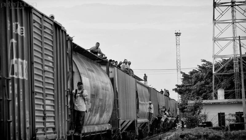 People sitting and standing on top of a moving freight train, with the Dari&eacute;n Gap landscape in the background.