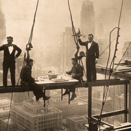 Vintage sepia-toned photo of construction workers having lunch on a steel beam high above a cityscape, with a waiter generously serving them.
