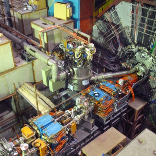 Interior of a particle physics laboratory showing a complex particle accelerator setup with multiple cables, detectors, and machinery designed to study glueball particles.