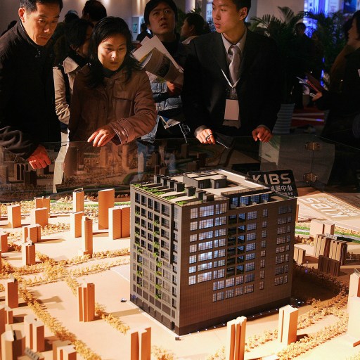 People examining a detailed architectural model of a building and its surrounding area at an exhibition, reflecting the impact of the Chinese economy on urban development.