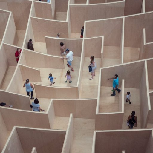 Visitors exploring why people get lost in a large, complex wooden maze installation in an indoor gallery setting.