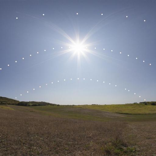 A composite image shows the sun's path in the sky at different times of the year over a grassy landscape, with three arches of sun positions represented by dots, illustrating the earliest solstice.