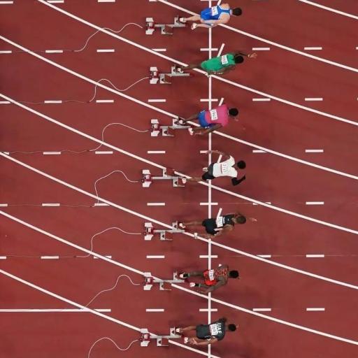 Overhead view of athletes in starting blocks on a track, preparing for the fastest 100 meters. Marked lanes and starting lines are visible.