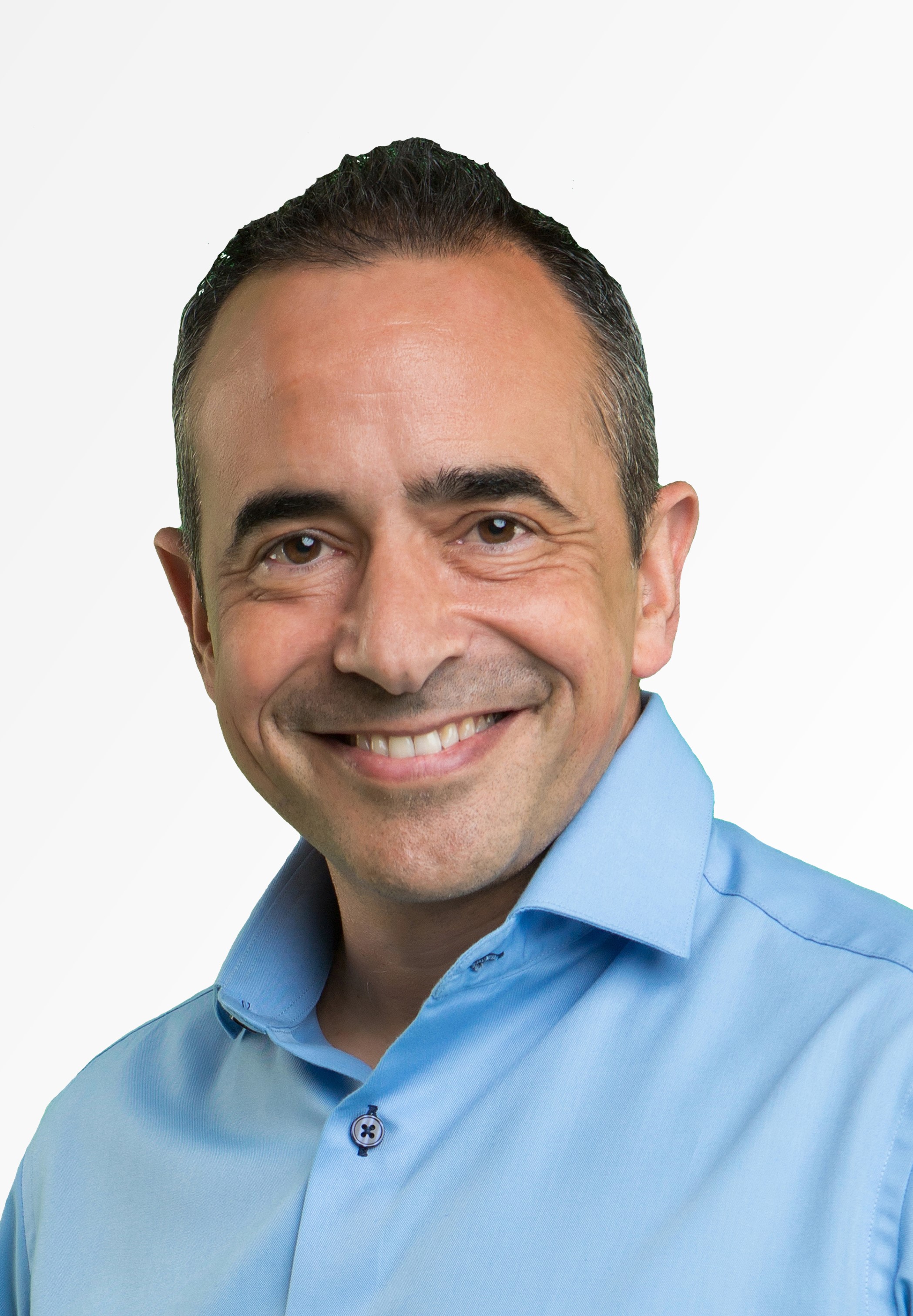 A man with short dark hair and a slight smile is wearing a light blue collared shirt against a plain white background.