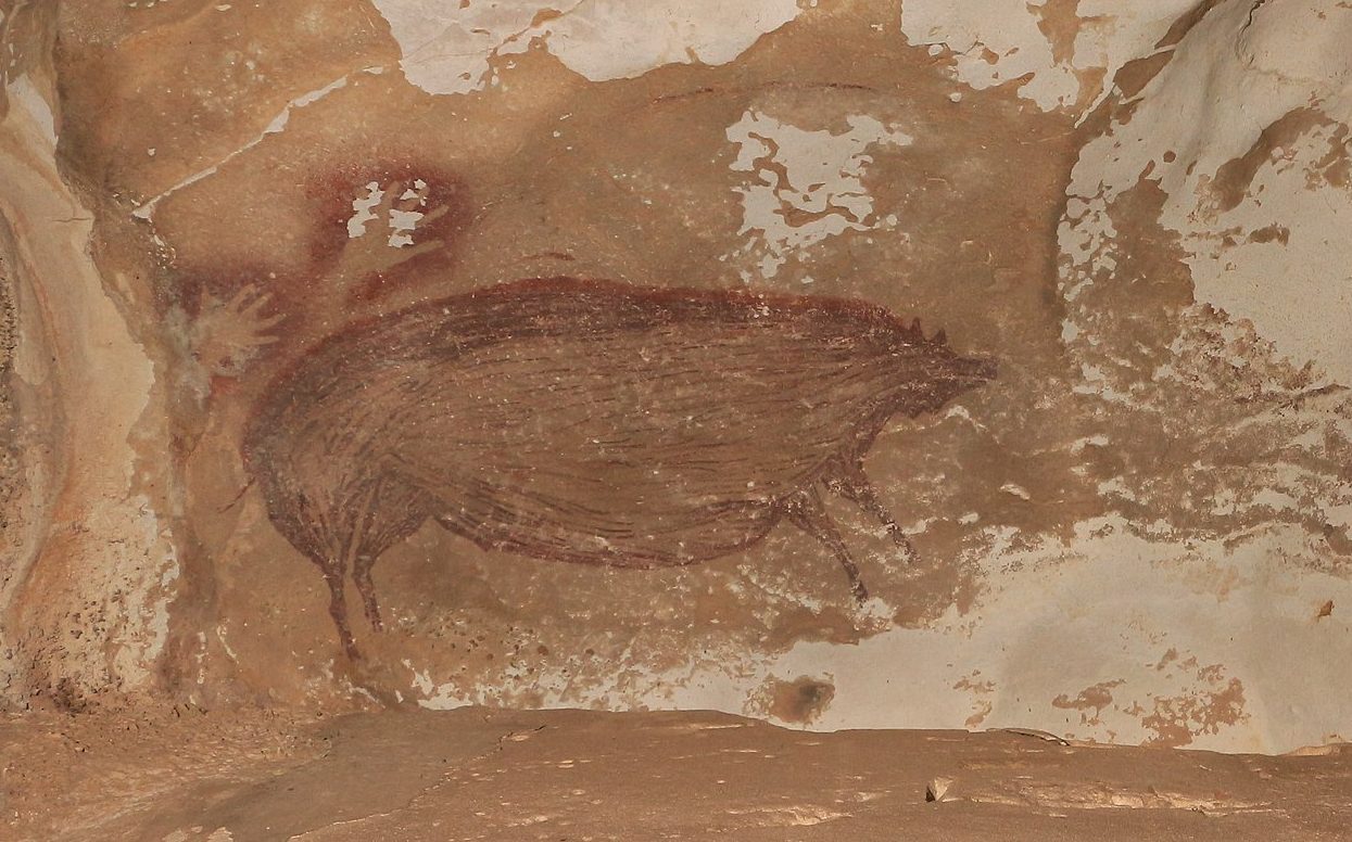 Ancient cave painting depicting animal figures, including what appears to be a bull and a bird, on a textured, brown and beige rock surface.