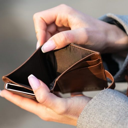 Person holding an open, empty brown wallet with both hands, outdoors.