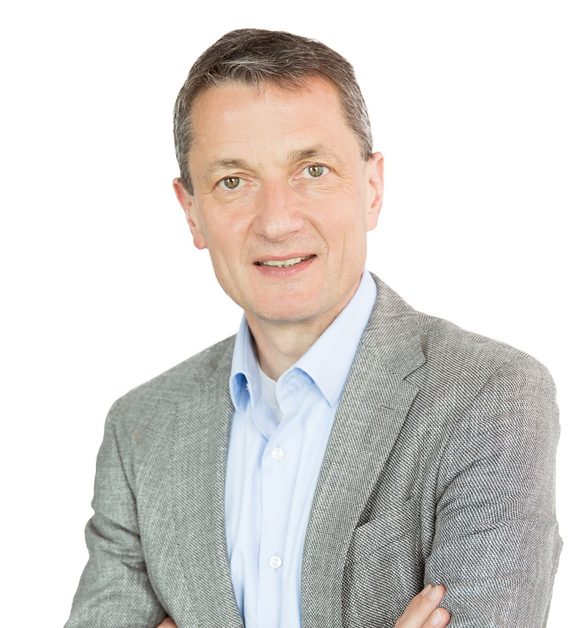 A man wearing a light gray blazer over a blue shirt stands with his arms crossed against a plain white background.