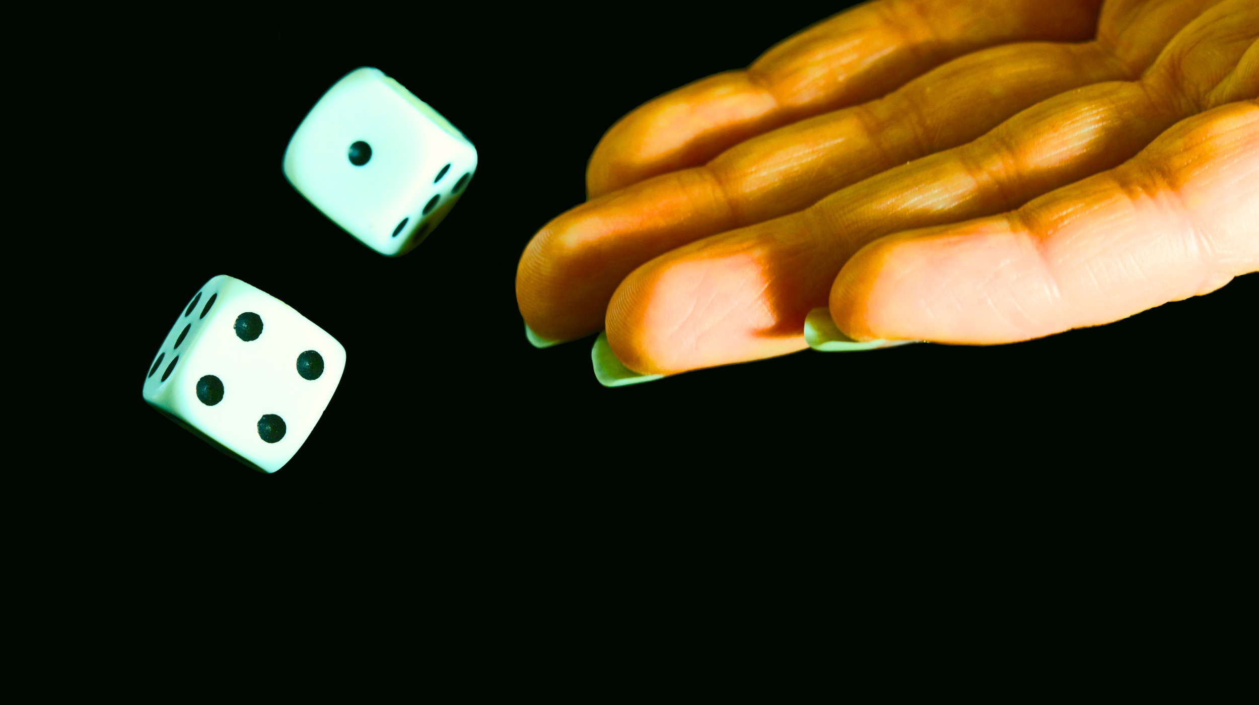 A hand is tossing two white dice with black dots against a dark background.