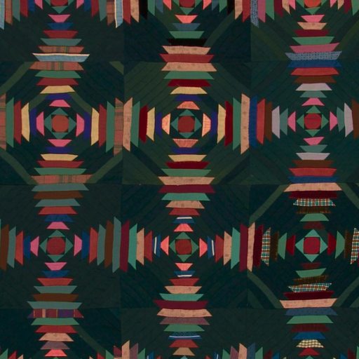 A geometric quilt with repeating concentric diamond and striped patterns in red, pink, orange, and blue tones on a dark background.