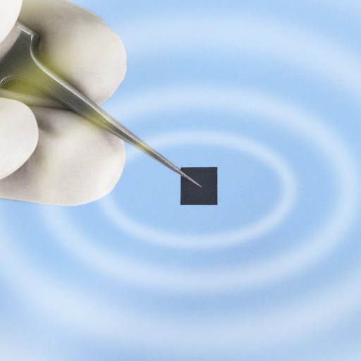 A hand holding tweezers grips a small black square against a blue background with concentric white circles.