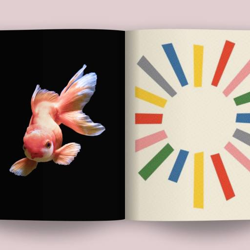 Open book showing a goldfish on the left page set against a black background and a colorful circular pattern on the right page, symbolizing the vibrancy of company culture. The book lies flat on a neutral surface.