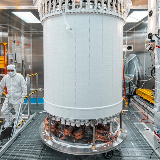 A technician in a cleanroom suit works by a large cylindrical piece of equipment in a high-tech laboratory setting with industrial tools and machinery.