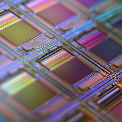 Close-up of a colorful microchip wafer with geometric patterns and reflective surfaces.