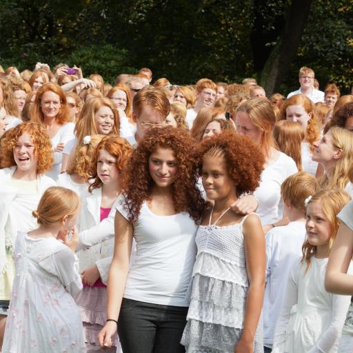 A large group of people with red hair gather outdoors, many wearing white clothing.