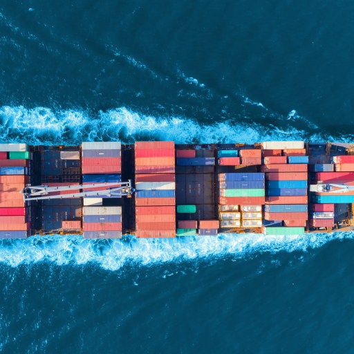 Aerial view of a large cargo ship with multicolored containers navigating through deep blue ocean waters.