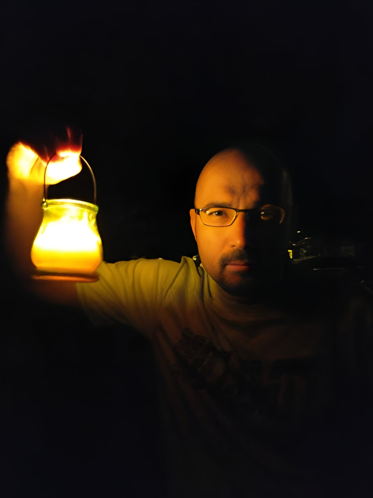 A person holding a glowing lantern in the dark, partially illuminating their face.