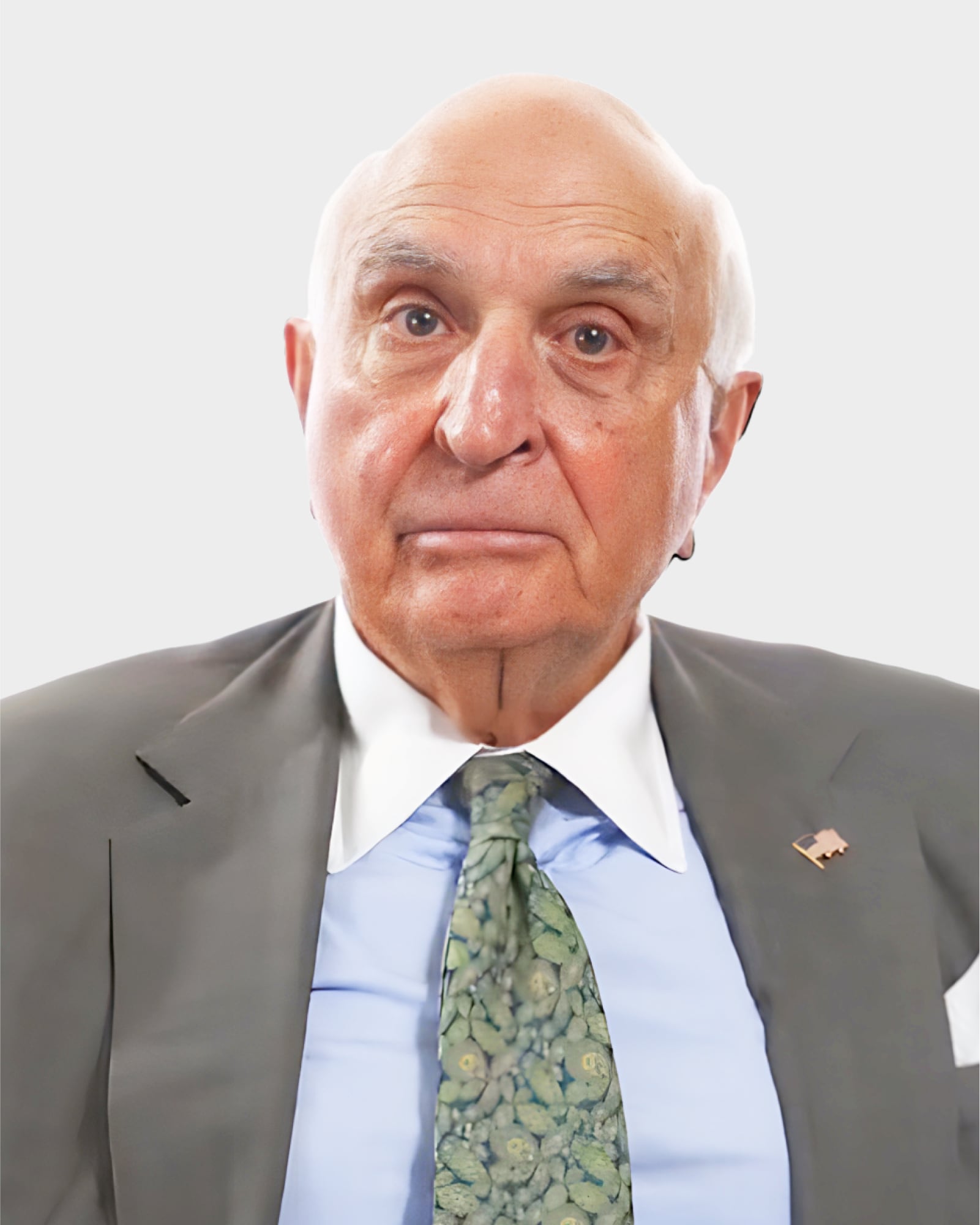 An older man in a suit and floral tie looks at the camera against a plain white background.