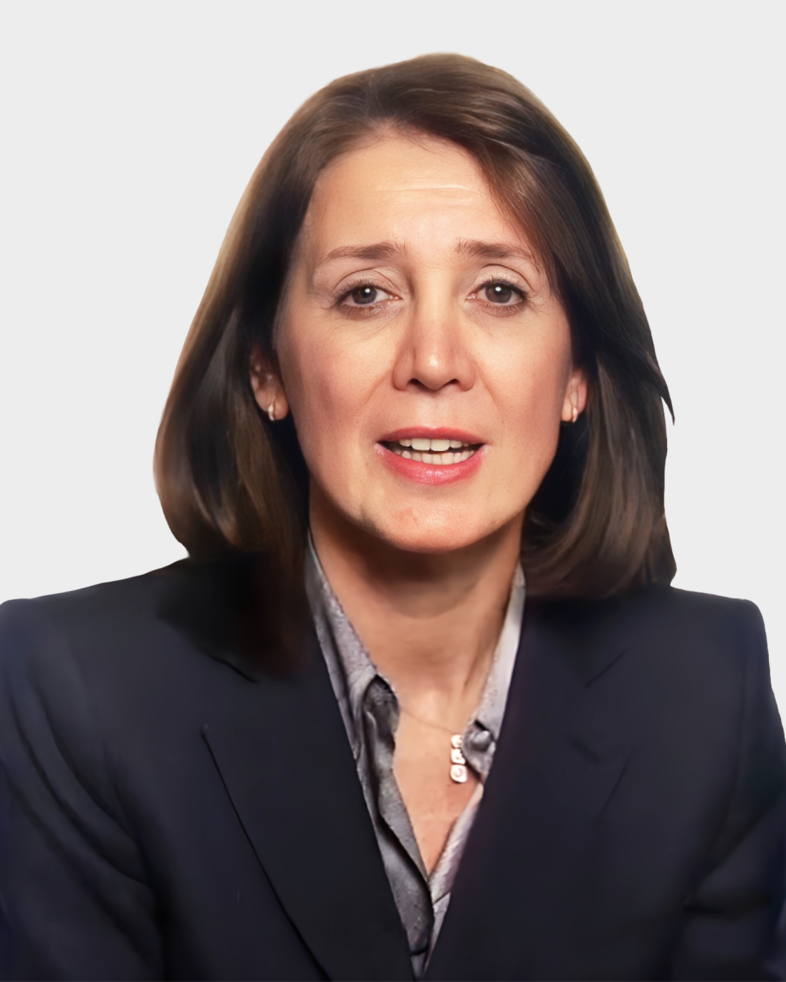 A woman with brown hair is wearing a dark blazer and light-colored blouse, speaking against a plain white background.