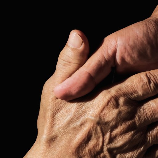 A hand clasps an older, wrinkled hand against a black background, symbolizing care and support.
