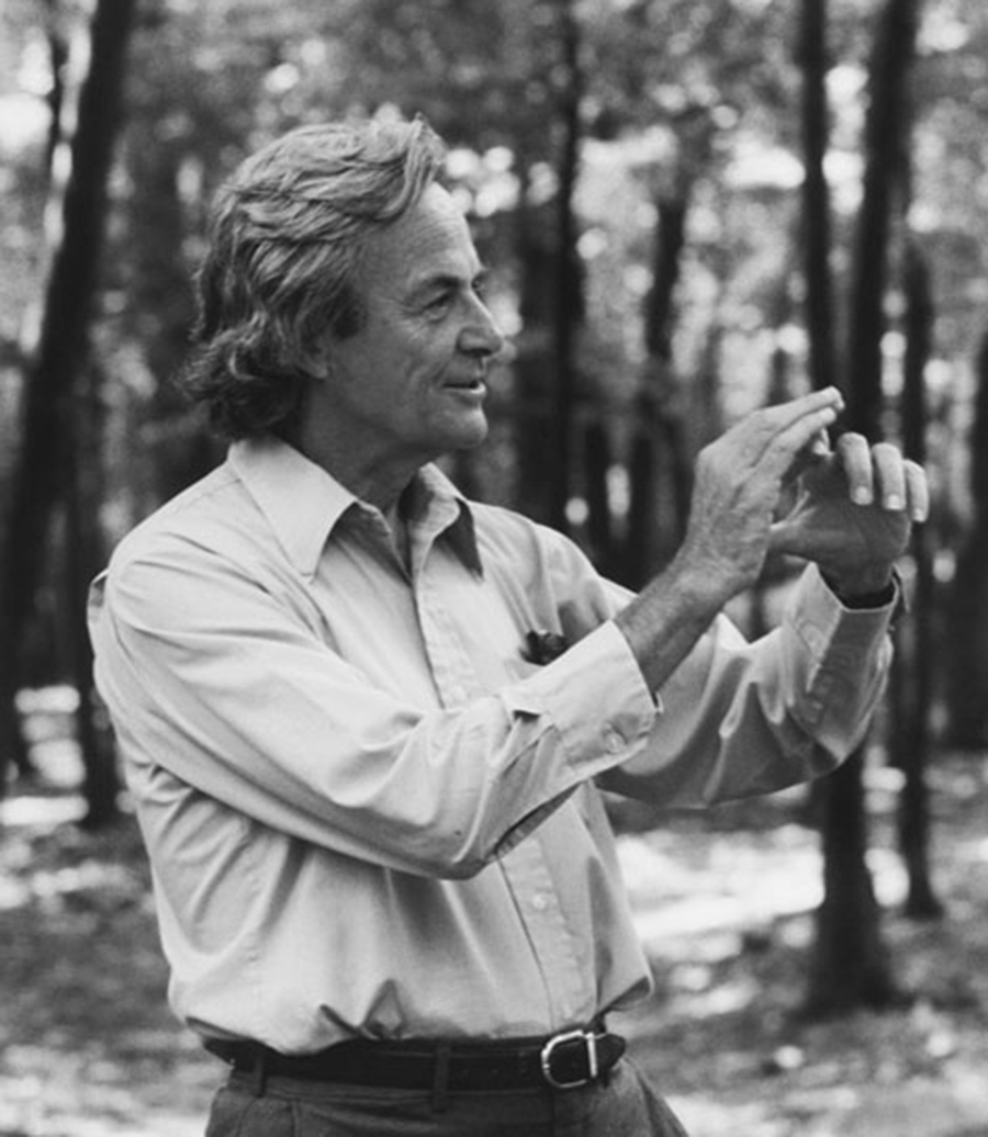 Black and white photo of a man outside, gesturing with his hands, surrounded by trees.