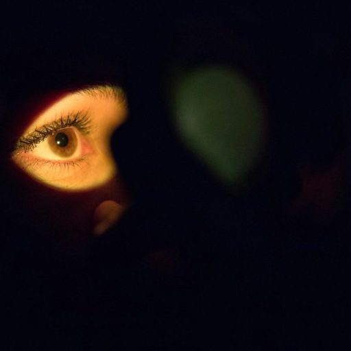 A single eye illuminated in the dark with a warm light.