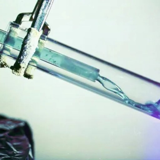 A test tube with a clamp holds a clear liquid and a glass rod inside, evoking the precision of nuclear research, set against a neutral background.