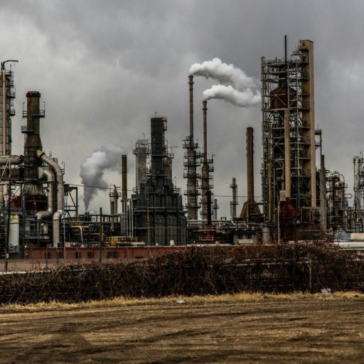 Industrial landscape featuring large smokestacks and various structures of an oil refinery, some incorporating cutting-edge carbon removal technology, set under a cloudy sky.