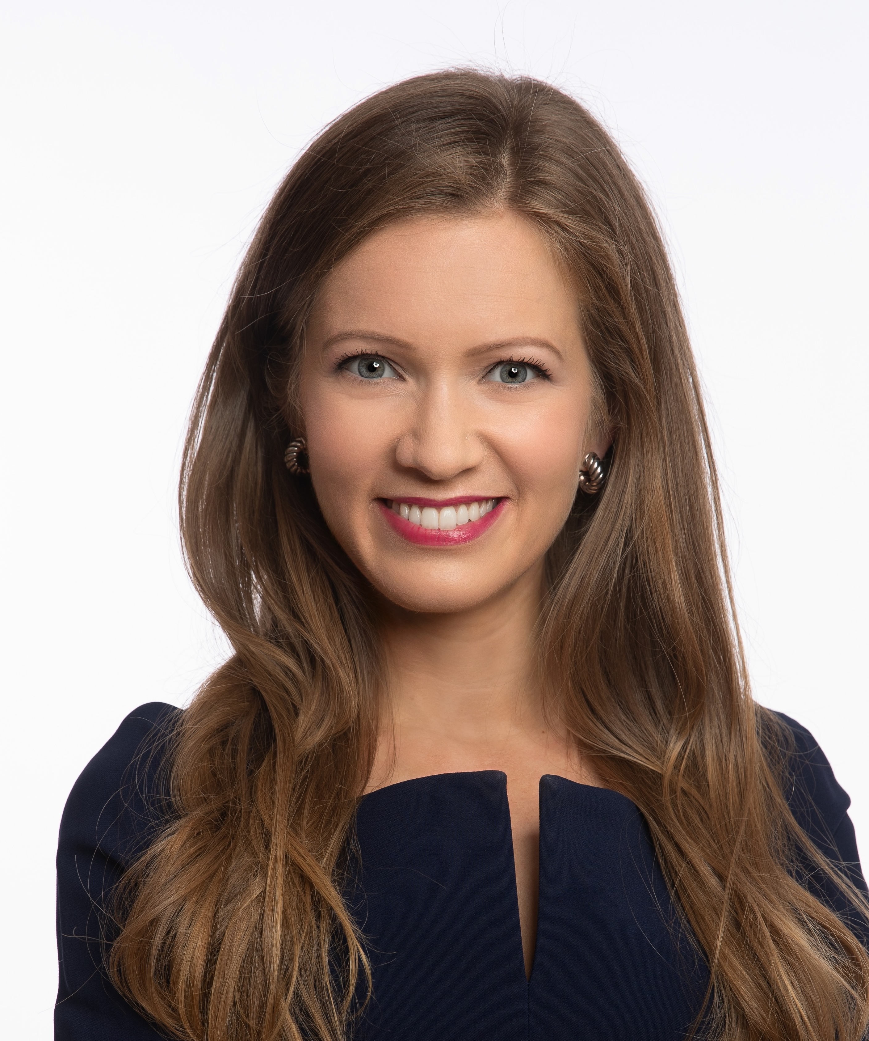 A woman with long brown hair smiles, wearing a dark blue outfit.