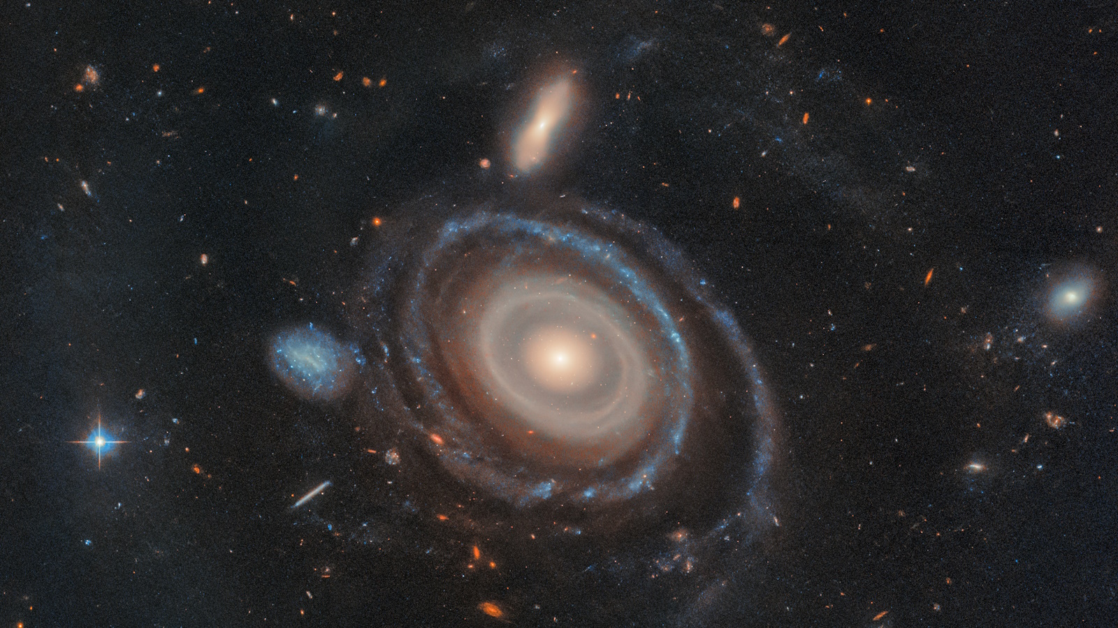 A spiral galaxy with a luminous core, surrounded by swirling arms and smaller galaxies, forms a mesmerizing bullseye ring galaxy, set against a backdrop of stars in space.