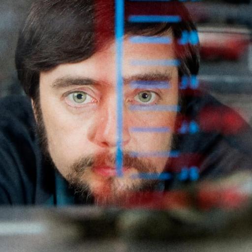 Man peering through a glass container with measurement markings, focused expression, blurred foreground.