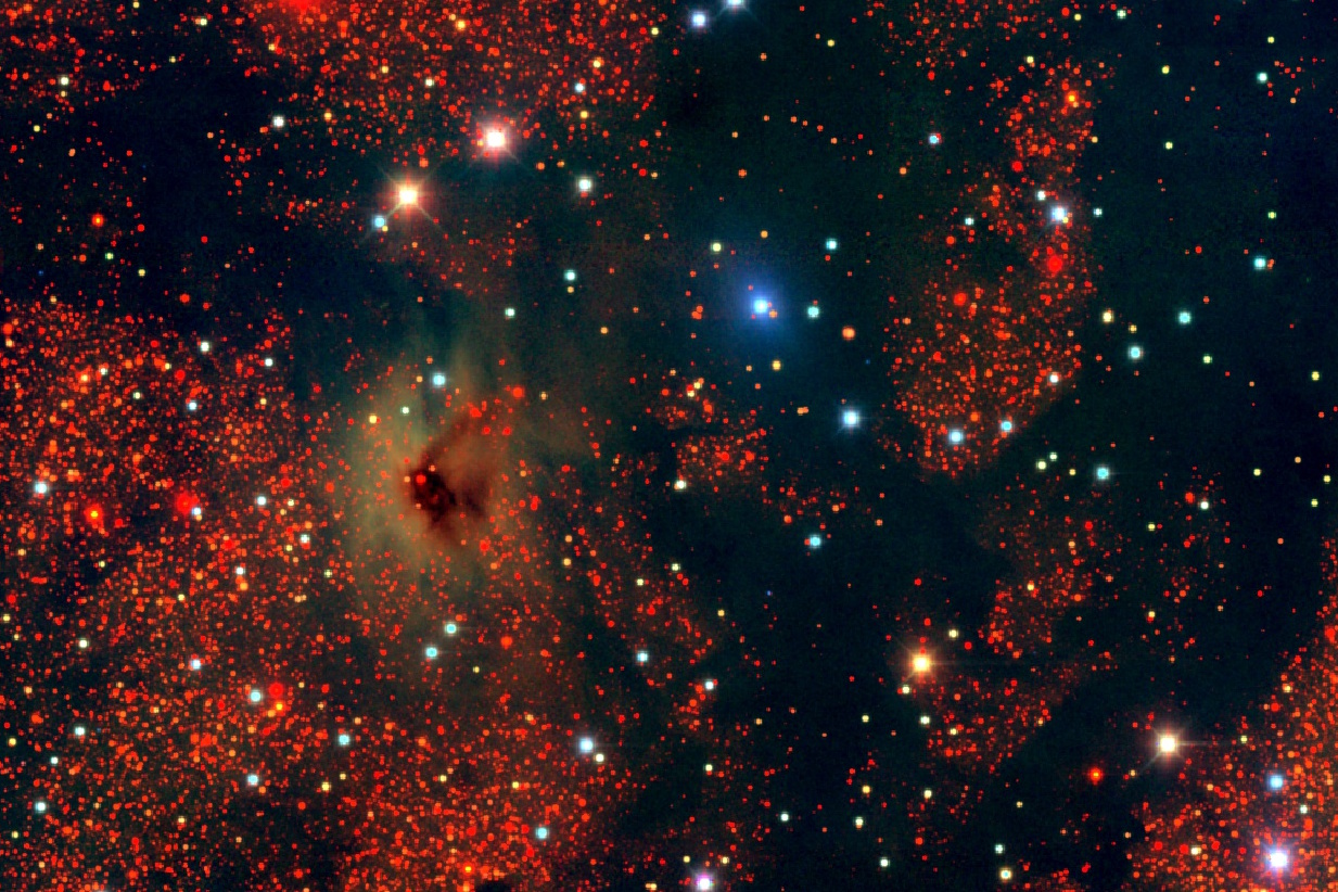 A dense starfield, with various colored stars shimmering through a dark cloud-like formation, lies against a deep black background in the mysterious zone of avoidance.