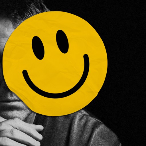 A person sits in darkness, frowning, partially obscured by a large yellow smiley face sticker covering part of their face.