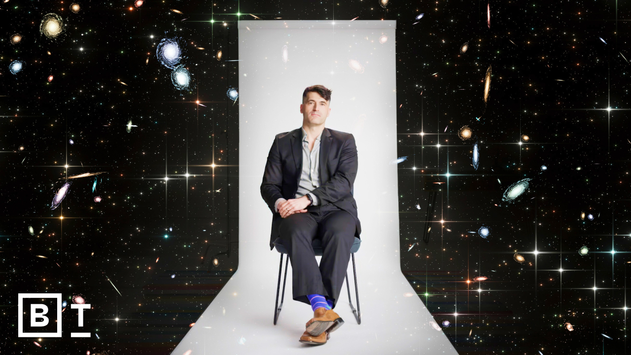 A person in a suit sits on a chair against a cosmic background with galaxies and stars.