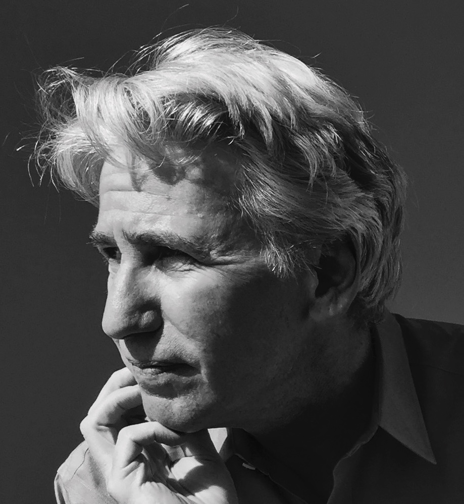 A black-and-white photo of a person with light hair, looking to the side, hand resting on the chin, with a contemplative expression.