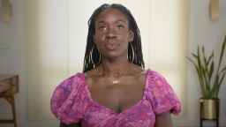 Person wearing a purple floral top and hoop earrings, looking upwards. A plant and a wooden table are in the background.
