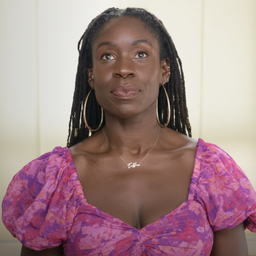 Person wearing a purple floral top and hoop earrings, looking upwards. A plant and a wooden table are in the background.