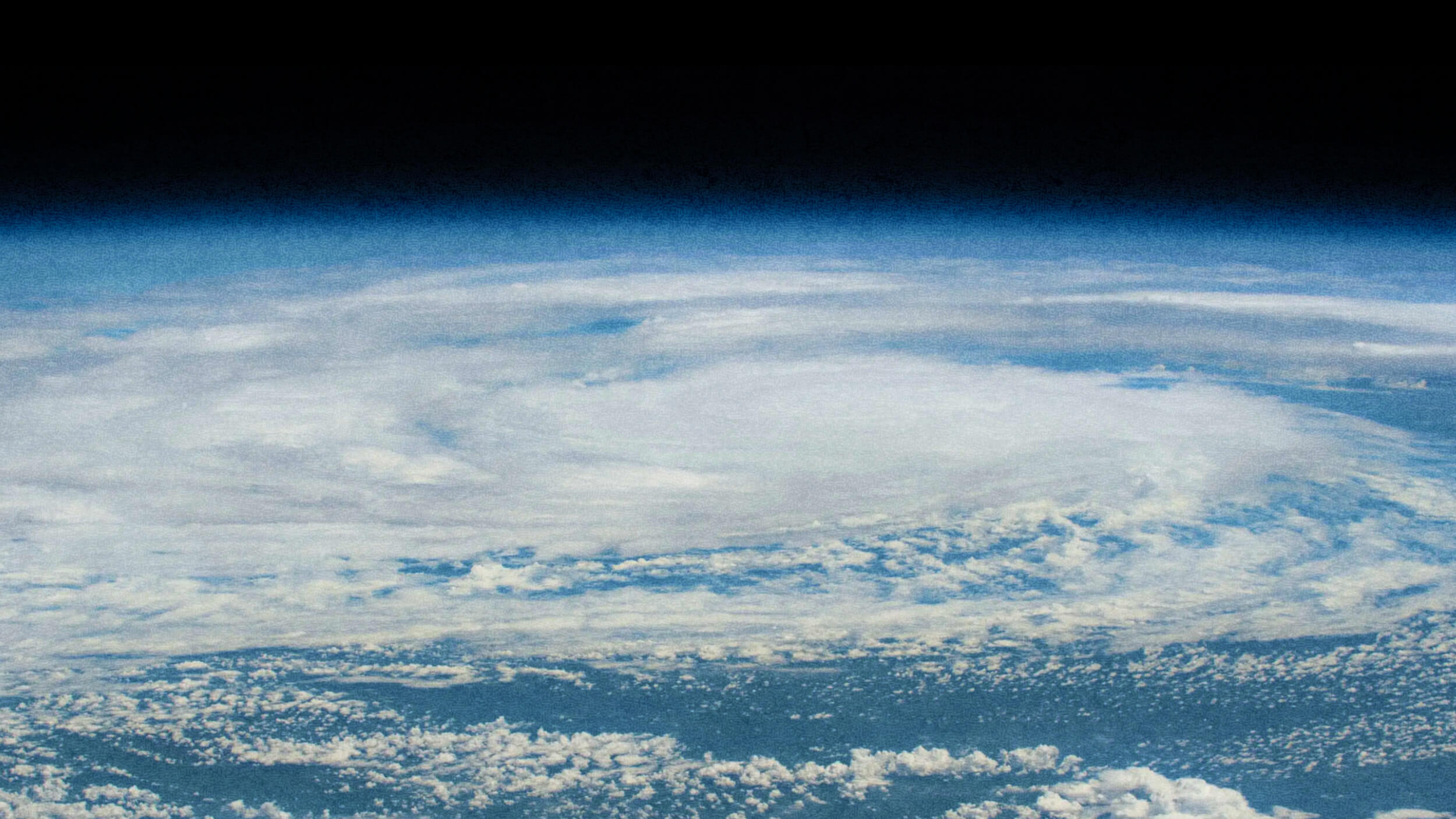From a vantage point reminiscent of Carl Zimmer's explorations, an aerial view captures a massive swirling cloud formation over Earth, resembling a hurricane or cyclone against the infinite darkness of space.