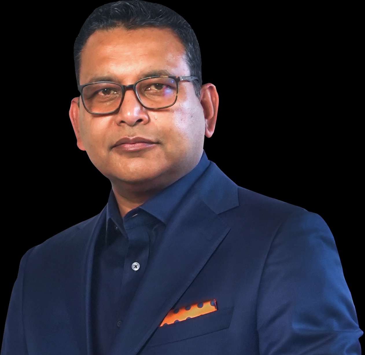 A man wearing glasses and a blue suit with an orange pocket square against a black background.